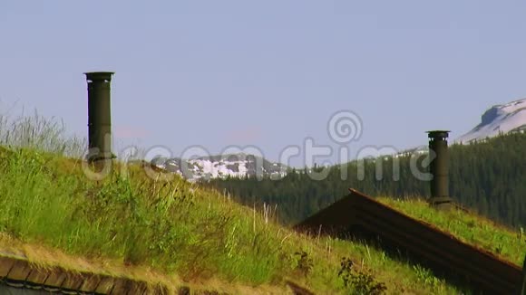 有两根黑色的管子的小房子的屋顶上来的绿草夏天山脉视频的预览图