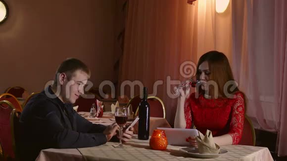 男人和女孩在咖啡馆里带着智能手机和平板电脑晚上爱浪漫的情人节4K视频的预览图