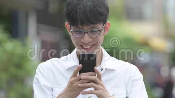 年轻快乐的亚洲商人在户外使用电话时面带微笑视频的预览图