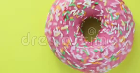 明亮和五颜六色的甜甜圈特写镜头旋转在黄色的背景美味的甜面圈在旋转视频的预览图