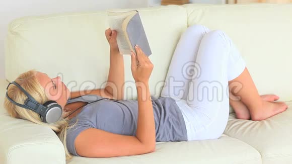 女人躺在沙发上一边用耳机听音乐一边看书视频的预览图