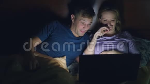 夫妻男人和女人在睡觉前在卧室的床上用笔记本电脑看电影看一部令人兴奋的电影视频的预览图