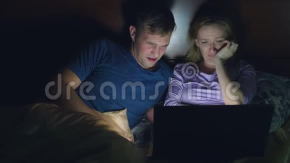夫妻男人和女人在睡觉前在卧室的床上用笔记本电脑看电影看一部令人兴奋的电影视频的预览图