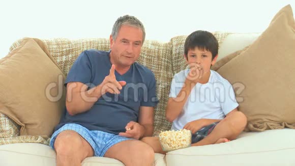 一个男人和他的孙子在电视上看比赛视频的预览图