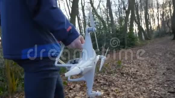 一个穿着蓝色夹克的人带着一架无人机缓慢地穿过森林视频的预览图