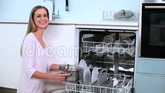 金发女人把盘子放进洗碗机在厨房里竖起大拇指视频的预览图