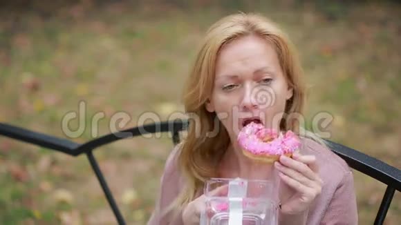 公园里的金发女孩吃甜甜圈户外女人吃甜面包视频的预览图