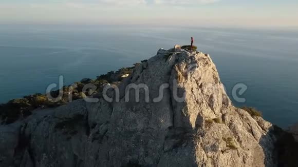 鸟瞰一位年轻女子站在山顶靠海的景色在美丽的风景中登上顶峰的女士视频的预览图