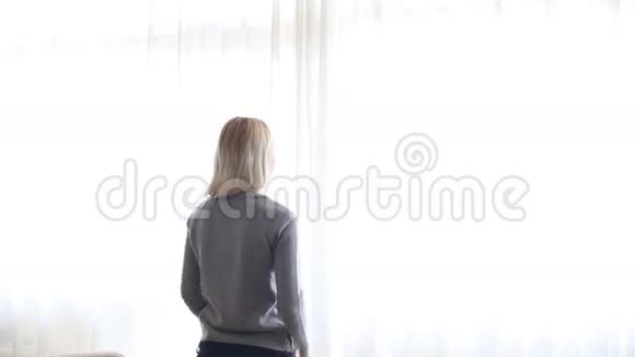 美女打开大窗户上的窗帘让光线进入房间望着窗外视频的预览图