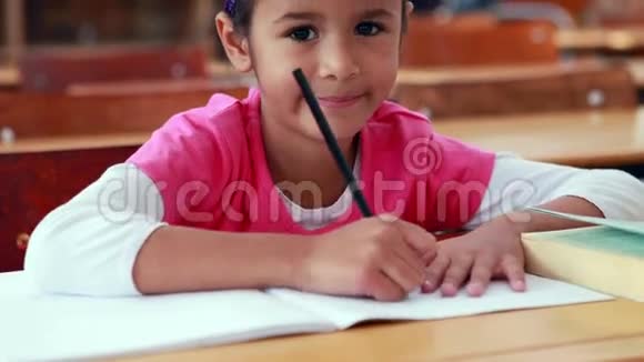 教室里可爱的小女孩在书上涂着颜色对着镜头微笑视频的预览图