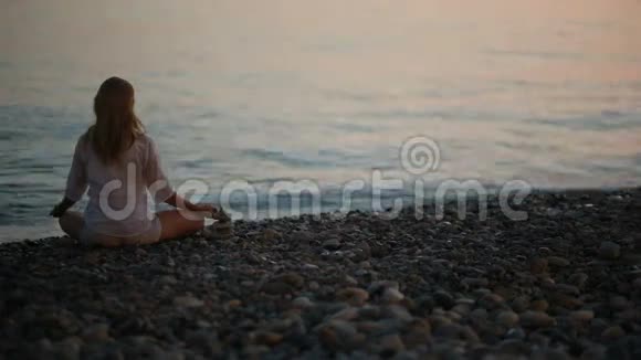日落时分年轻女子在海滩上练习瑜伽平静的大海视频的预览图