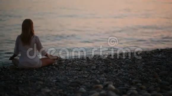 日落时分年轻女子在海滩上练习瑜伽平静的大海视频的预览图