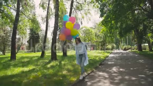 在阳光明媚的公园里散步时一个快乐顽皮的女孩摆着五颜六色的气球视频的预览图