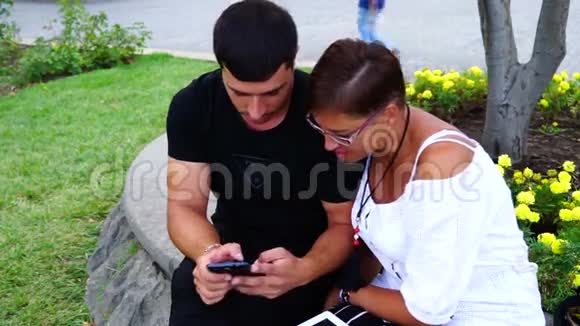 一对夫妇坐在花园的长凳上使用平板电脑和智能手机他们正对着镜头视频的预览图