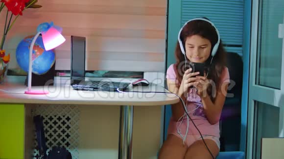 小女孩在智能手机上耳机听音乐青少年女孩在社交中翻阅播放列表音乐视频的预览图