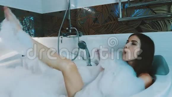 布鲁内特年轻女孩在浴室里洗了满是泡沫的澡从泡沫中吹出气泡视频的预览图