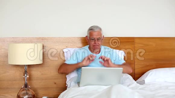 坐在床上的老人用笔记本电脑和欢呼视频的预览图