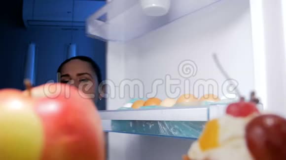饥饿的女人晚上从冰箱里拿甜蛋糕的4K镜头视频的预览图