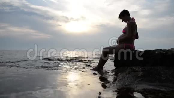 穿着泳衣的孕妇坐在侧面抱着肿胀的肚子视频的预览图