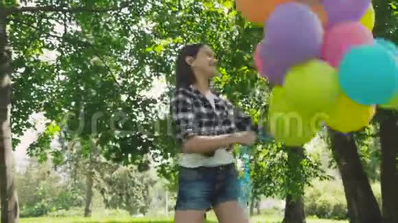 在阳光明媚的公园里散步时快乐的顽皮的女孩摆出五颜六色的气球4K视频的预览图