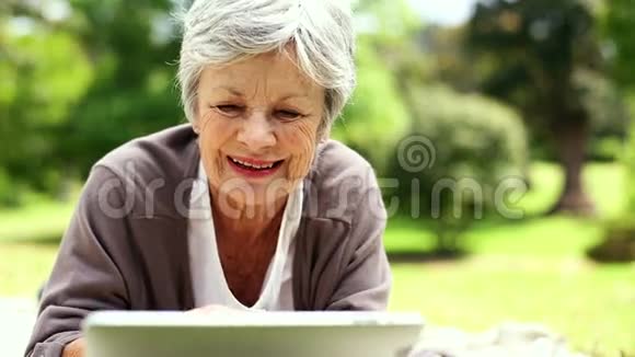 快乐的老年妇女使用她的平板电脑在公园放松视频的预览图
