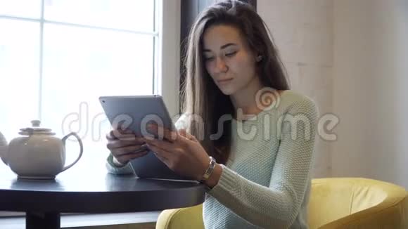 年轻的黑发女孩坐在靠近窗户的桌子上在平板电脑上工作视频的预览图