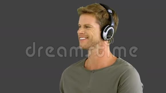 有魅力的男人带着耳机在灰色屏幕上听音乐视频的预览图