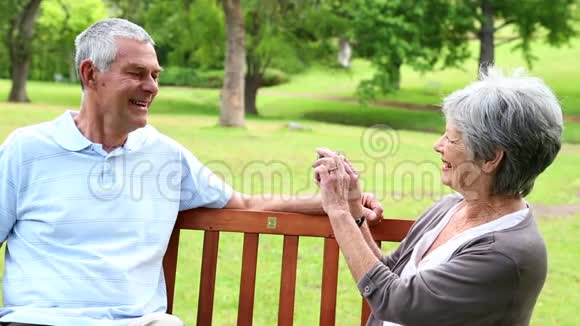 退休夫妇坐在公园长椅上拍照视频的预览图