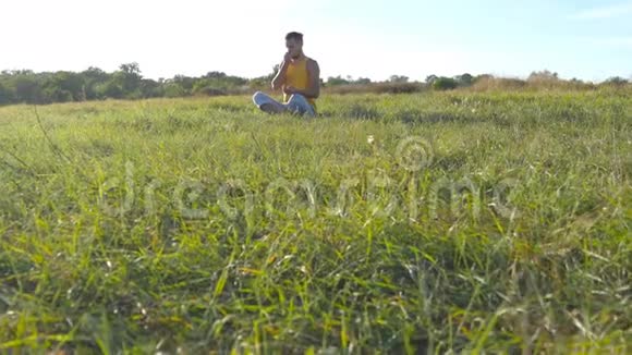年轻男子坐在瑜伽姿势在草地上的绿草和冥想肌肉男在莲花中放松的姿势视频的预览图