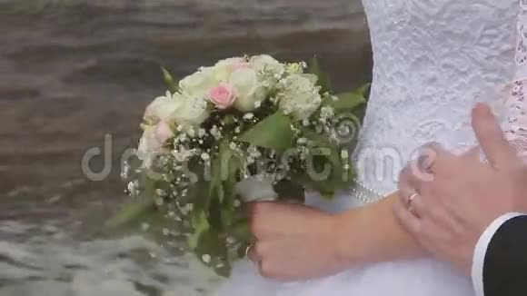 新郎拥抱新娘在海边抚摸手臂婚礼日视频的预览图