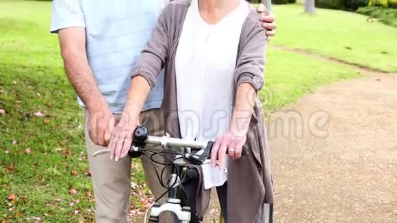 退休夫妇和一个骑自行车的女人一起站在公园里视频的预览图