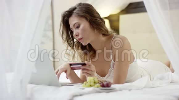 女人躺在床上用她的笔记本电脑和信用卡视频的预览图