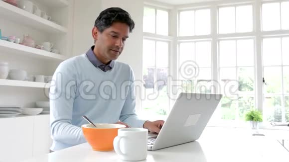 印度男人一边吃早餐一边用笔记本电脑视频的预览图