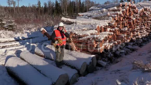 冬天伐木工人在一堆木头附近用智能手机聊天视频的预览图