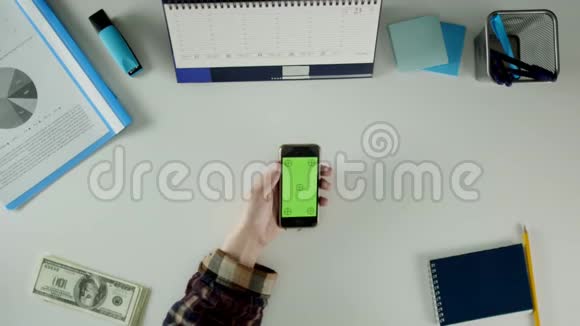 一个男人坐在他的办公桌前用他的手机桌子上有办公用品视频的预览图