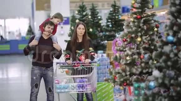 漂亮的一家人带着超市的购物车走下大厅选择圣诞玩具和圣诞礼物视频的预览图