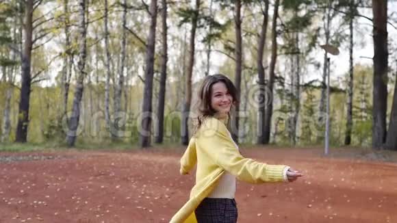 一个穿着黄色毛衣的年轻女子在秋天公园散步黑发女人在森林里跳跃和跳舞浪漫浪漫视频的预览图