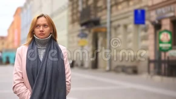 一个穿着粉红色外套和毛衣的疲惫的女人站在拥挤的街道中间从寒冷中退缩出来视频的预览图