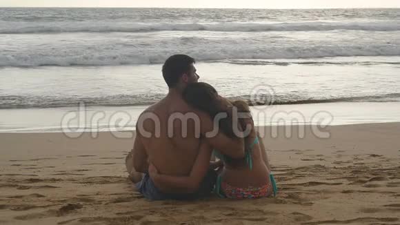 年轻的浪漫夫妇正在享受美丽的日落坐在海滩上拥抱一个女人和一个男人坐在一起视频的预览图