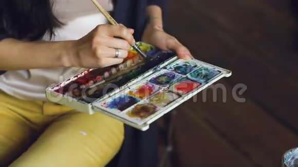 年轻的女画家用水彩画和画笔混合色彩来画图画视频的预览图