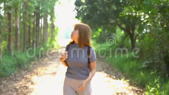 快乐的年轻亚洲女性旅行者带着背包在森林里散步视频的预览图