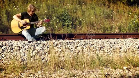 坐在铁路上的年轻男吉他手视频的预览图