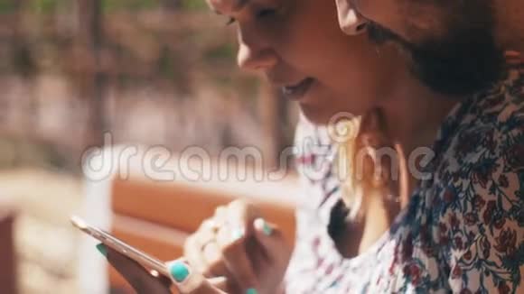 年轻的恋爱夫妇使用智能手机坐在长凳上夏天刮风的日子快乐视频的预览图