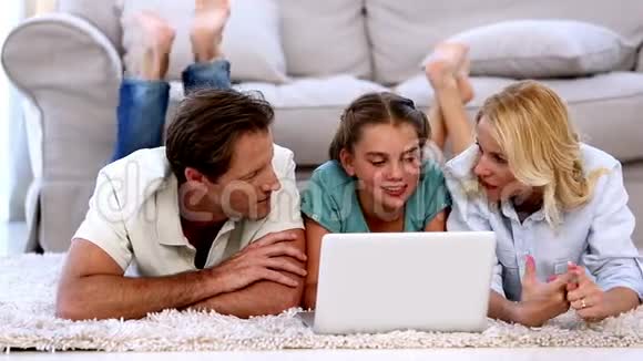 父母和女儿在地板上愉快地使用笔记本电脑视频的预览图