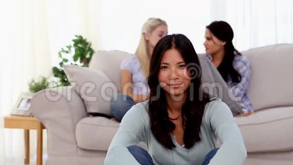 微笑的女人坐在地板上朋友们在后面聊天视频的预览图