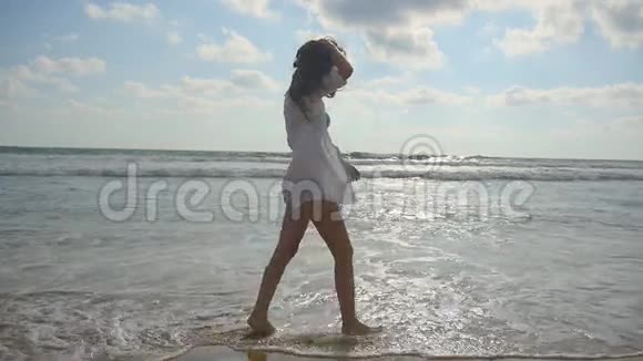 快乐的女人光着脚在海边的沙滩上散步年轻漂亮的女孩享受生活和乐趣视频的预览图