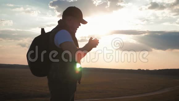 一个带背包的剪影青年游客使用手机在夕阳的光芒中慢动作旅费视频的预览图