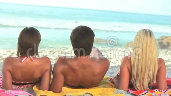 三个朋友坐在沙滩上的毛巾上视频的预览图