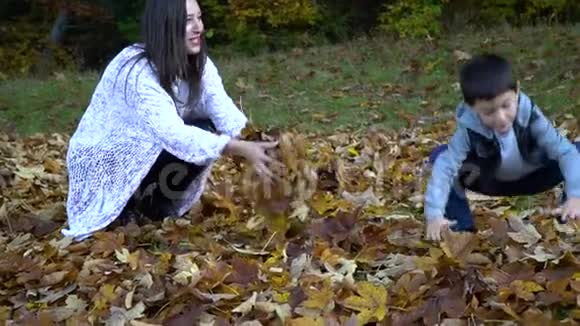 年轻漂亮的妈妈和她的小儿子在秋天的森林里玩得很开心他们跳起来把树叶扔到空中他们视频的预览图