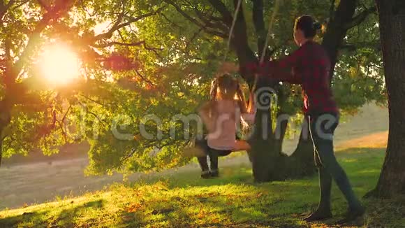 年轻的母亲和她的孩子女儿在秋千上荡秋千在户外度过了一个温暖的秋天快乐的爱视频的预览图